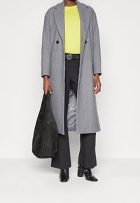 Gray wool blend coat with a double-breasted design, worn over a bright yellow top and black trousers; holding a dark grey bag.