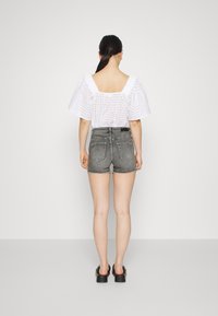 Blusa blanca bordada con mangas abullonadas, combinada con pantalones cortos de mezclilla gris de tiro alto. La modelo lleva sandalias negras sin tacón. Diseño simple y limpio.