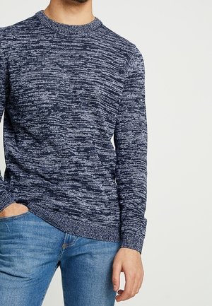Pull en maille bleu marine avec un motif texturé et chiné. Il a un col rond et des poignets ajustés. Assorti avec un jean bleu clair.