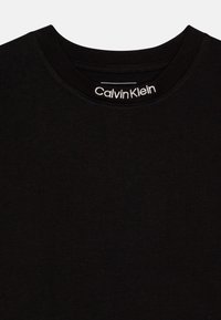 Juodas medvilnės marškinėliai su apvaliu kaklu. Yra baltas „Calvin Klein“ logotipas, siuvinėjamas kaklo vietoje. Lygus paviršius, klasikinis dizainas.