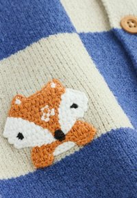Knitted cardigan with blue and cream checkered pattern; features an embroidered orange fox with white accents and button closure.
