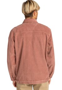 Giacca di velluto a coste rosa con colletto a punta, maniche lunghe e chiusura a bottoni ai polsini e all'orlo. Tessuto testurizzato con coste verticali.