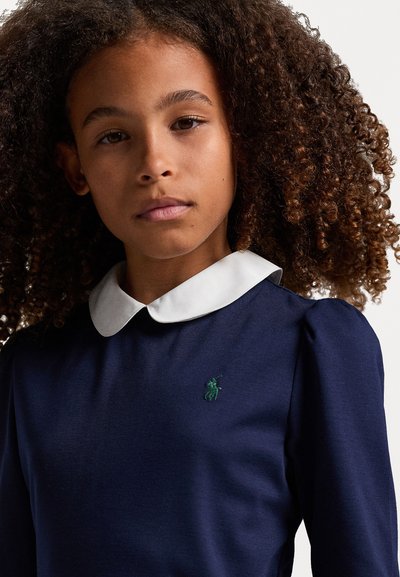 Tamsiai mėlyna suknelė su ilgomis rankovėmis, baltu koloriumi ir subtiliu žaliu išsiuvinėtu logotipu krūtinėje; glotni tekstūra ir pritaikytas kirpimas.