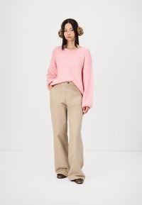 Maglione rosa a maglia con maniche lunghe, pantaloni beige a gamba larga e calzature con stampa animalier; gli accessori includono cuffie marroni con stampa leopardata.
