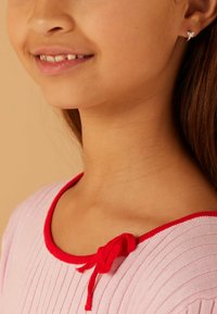 Haut rose côtelé avec un col rouge et un détail de nœud. Design simple, texture douce, avec des coutures subtiles visibles le long du col.