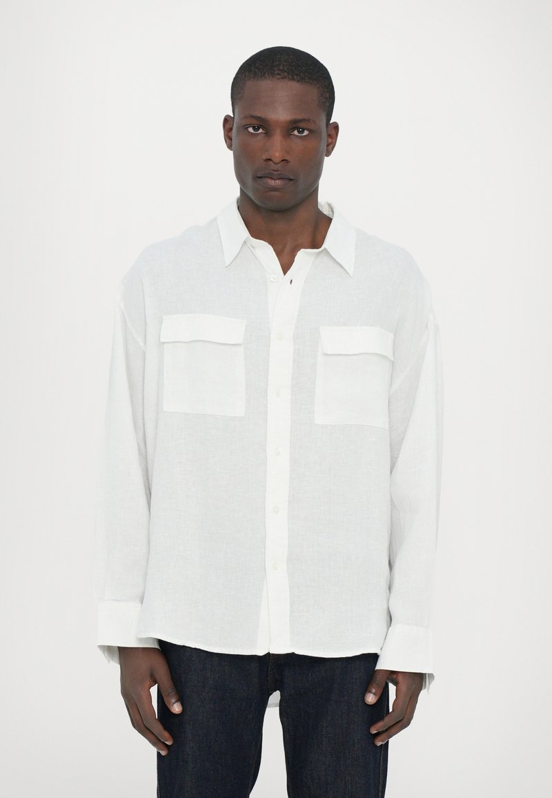 Witte linnen blouse met een ontspannen pasvorm, knoopsluiting aan de voorkant en twee borstzakken. Lange mouwen met opvouwbare manchetten. Effen structuur.