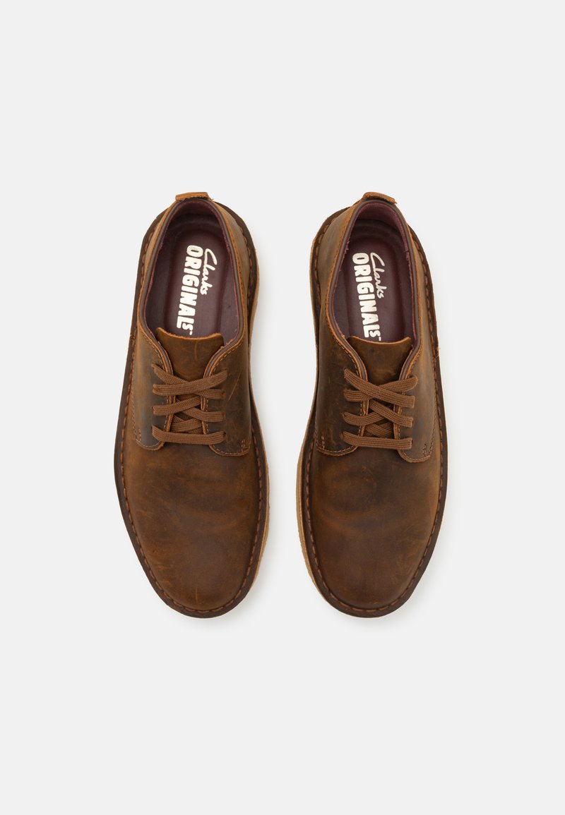 Zapatos de cuero marrón con una textura suave, punta redonda y diseño de cordones. Presentan detalles de costura y una plantilla acolchada etiquetada como "Clarks ORIGINALS".