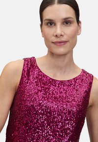 Fuchsia mouwloos topje bedekt met pailletten, met een ronde halslijn en een gladde textuur, die het licht weerkaatst en een glinsterend effect creëert.