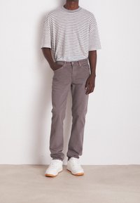 Šedé a bílé pruhované oversized tričko, světle šedé kalhoty a bílé tenisky s gumovou podrážkou. Jednoduchý design, volný střih, minimální detaily.