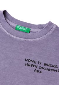 Lilia bluzka z okrągłym dekoltem i krótkim rękawem, z czarnym napisem na przodzie "DOM JEST TAM, GDZIE SĄ SZCZĘŚLIWE SMOKI". Zielona metka marki.