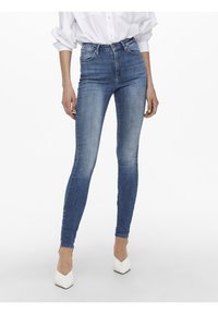 Höga blå skinny jeans i en bleknad tvätt, med klassisk femfickstil och en åtsittande passform, kombinerat med vita högklackade skor.