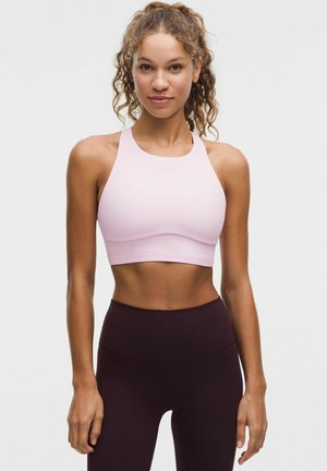 Lichtroze sportbh met een hoge hals en een gladde textuur, gecombineerd met donkerpaarse hoge taille leggings. Minimalistisch ontwerp.