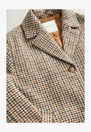 Brązowy i biały płaszcz w wzór houndstooth z pikowaną podszewką i zapięciem na guziki. Posiada wycięty kołnierz oraz teksturowany materiał.