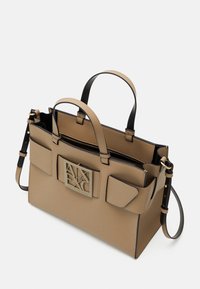 Béžová strukturovaná kabelka s černými doplňky, dvěma vrchními uchy, odnímatelným popruhem, přední kovovou destičkou s logem a dvěma vnějšími kapsami. Uzavírání na zip.