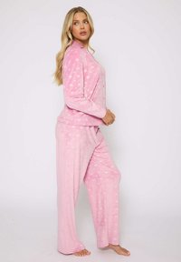 Completo Pigiama Rosa realizzato in stoffa morbida, caratterizzato da una camicia a maniche lunghe con bottoni e motivo a cuori, abbinato a pantaloni con vestibilità comoda.