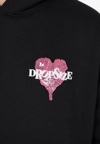 Black hoodie with a pink dripping heart graphic and white text "Dropsize" across the heart on the chest.