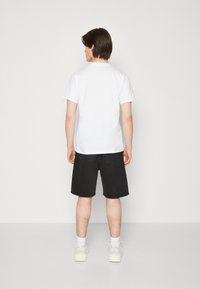 Camiseta blanca de algodón y pantalones cortos de mezclilla negros, combinados con zapatillas blancas. La camiseta es sencilla, mientras que los pantalones cortos tienen un corte holgado.