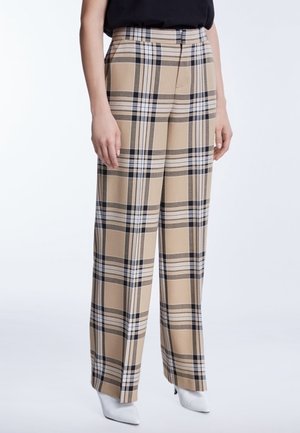 Pantalon large à carreaux beige, noir et blanc, porté avec un haut noir et des chaussures à talons pointues blanches.