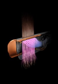 Piastra per capelli con corpo trasparente, dettagli in rame e flussi d'aria viola che modellano capelli lunghi, lisci e castani.