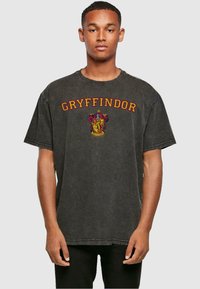 Camiseta negra de gran tamaño con la inscripción "GRYFFINDOR" en letras rojas y un escudo de Gryffindor en el centro. Material de algodón, corte holgado, mangas cortas.