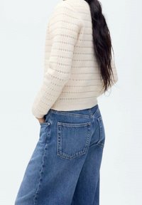 Pull en crème tricoté avec une texture rayée, associé à un jean large à taille haute bleu avec des poches arrière et une finition en denim classique.
