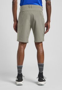 Shorts gris clair avec une texture lisse, une taille élastique et une coupe décontractée ; associés à des baskets noires et des chaussettes grises avec un logo.