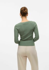 Haut à manches longues côtelé en vert doux, au design ajusté, avec un large décolleté et un tissu texturé, associé à un pantalon taille haute beige clair.