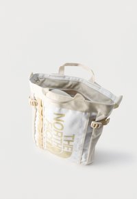 Μπεζ και λευκή τσάντα tote The North Face με επάνω λαβές, πλαϊνές αγκράφες, κλείσιμο με φερμουάρ και λογότυπο τυπωμένο στην μπροστινή τσέπη.