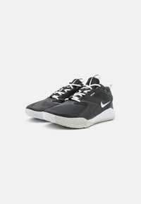 Čierne atletické topánky s textúrovaným zvrškom, bielymi šnúrkami a sivou gumovou podrážkou so vzorovanou podrážkou. Logo Nike na boku.