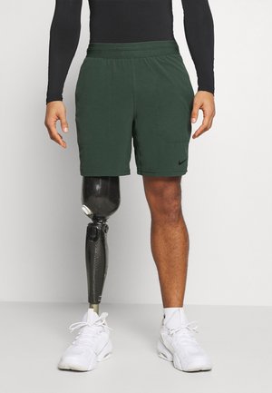 Zielone spodenki Nike z elastycznym pasem, dwoma bocznymi kieszeniami oraz czarnym logo. Nosi się je z dopasowaną, czarną bluzą z długim rękawem i białymi butami.