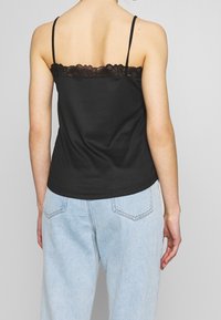 Top a canotta nera a coste con spalline sottili e bordo in pizzo. Indossato con jeans azzurri chiari e morbidi. Texture liscia, design aderente.