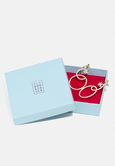 Pendientes en espiral dorados y blancos exhibidos en una caja azul claro con un interior rojo, con el logotipo de la marca en la parte superior.