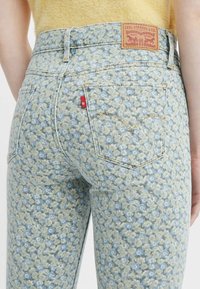 Jeans de denim con estampado floral en una combinación de colores azul claro y amarillo, que cuentan con bolsillos traseros y un parche de cuero con marca en la cinturilla.
