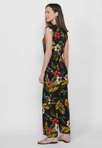 Jumpsuit floreale con sfondo nero, caratterizzato da vivaci motivi rossi, bianchi e verdi. Design senza maniche e dettaglio schiena aperta.