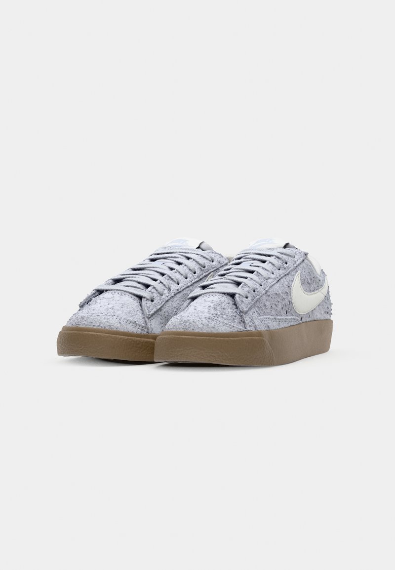 Baskets Nike avec un dessus gris texturé, logo blanc et semelle en caoutchouc marron. Présente un laçage traditionnel et une languette rembourrée.