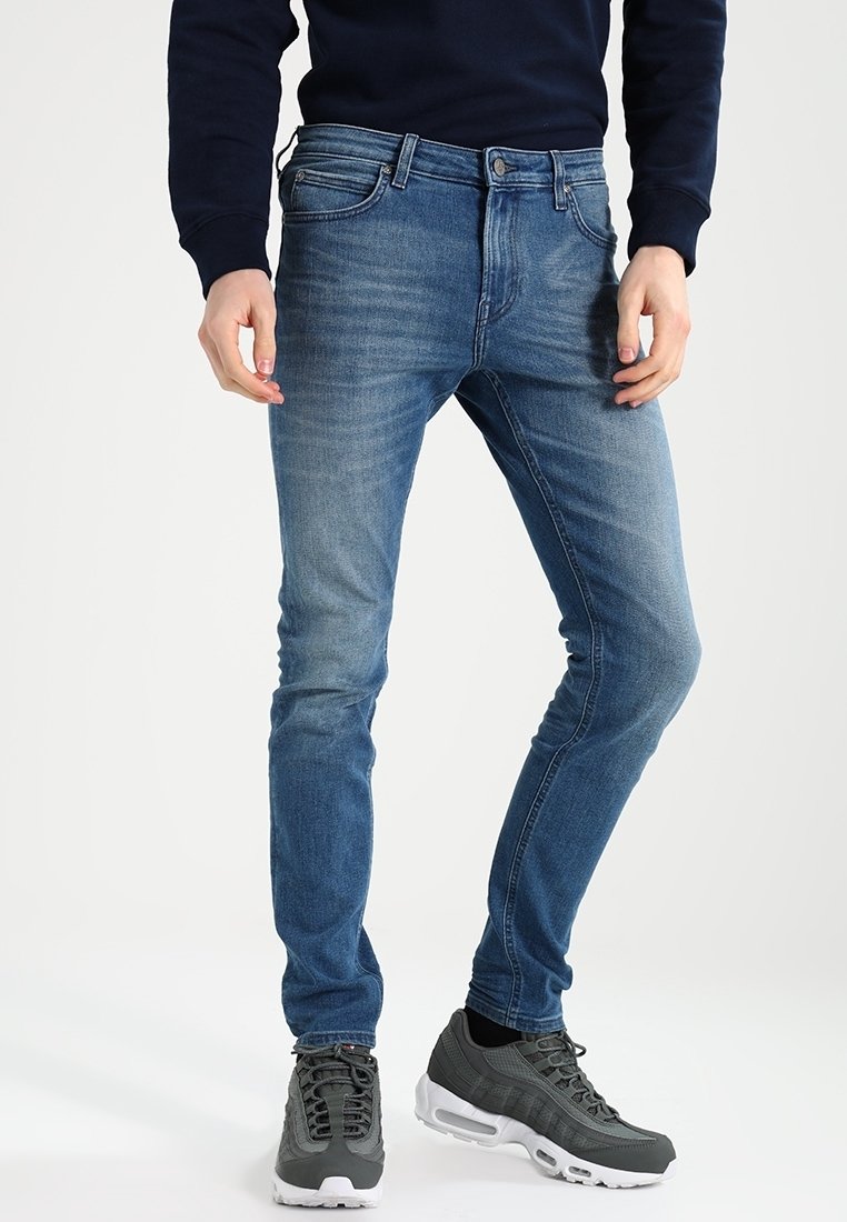 Blue denim jeans with a slim fit, light fading on thighs, five-pocket design, and contrast stitching, paired with gray athletic shoes.
