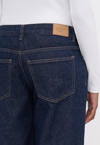 Mörkblå denimjeans med en läderetikett märkt "perfekta jeans" på baksidan, med två bakfickor och kontrasterande guldtråd.