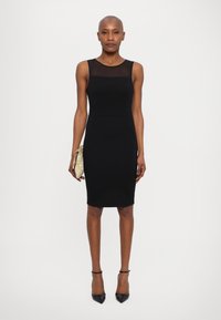Black sleeveless dress with a fitted silhouette, featuring a sheer neckline. Accompanied by a textured gold clutch and black pointed heels.