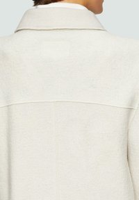 Lichtgrijze wollen jas met een kraag, voorzien van een gestructureerde stof en zichtbare naaddetails aan de achterkant.