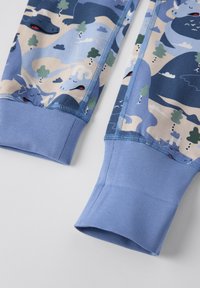 Blauwe stoffen broek met een speelse dinosaurustekening, compleet met wolken en bomen. De boorden hebben een solide blauwe textuur en zichtbare stikseldetails.