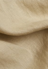 Vue rapprochée d'un tissu beige tissé avec une texture visible et des plis doux créant des ombres et de la profondeur.