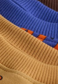 Tissu en maille côtelée multicolore avec une palette de couleurs jaune, bleue et marron, présentant des rayures horizontales et des textures contrastées.