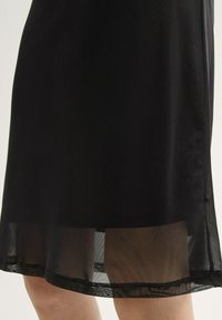 Schwarzes Kleid mit einem mehrschichtigen Design. Der Saum besteht aus einem durchsichtigen, netzartigen Stoff mit Spitzenakzenten, was der Silhouette Textur und Detail verleiht.