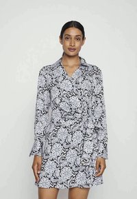 Vestido longo com padrão em preto e branco, de mangas compridas e gola, apresentando um design floral e detalhe na cintura com laço.