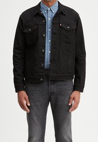Black denim jacket with two front pockets, silver buttons, and a collared neckline, layered over a light blue button-up shirt.