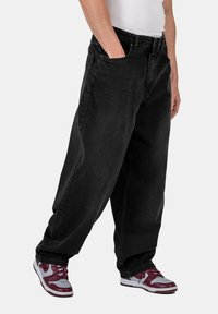 Jeans de mezclilla negra con un ajuste holgado, que cuentan con bolsillos laterales y cremallera. Combinados con zapatillas multicolores con detalles en blanco.