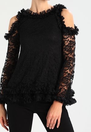 Schwarze Spitze Bluse mit kalten Schultern, gerafftem Ausschnitt und Bündchen, floralem Muster und Rüschensaum. Transparente lange Ärmel sorgen für Textur.