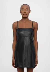 Rochie mini din piele neagră, cu decolteu pătrat și bretele subțiri. Are un design mulat și detalii de cusătură subtile. Textură netedă.