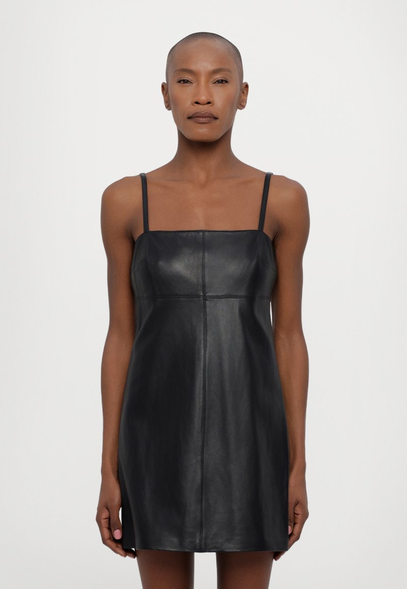 Rochie mini din piele neagră, cu decolteu pătrat și bretele subțiri. Are un design mulat și detalii de cusătură subtile. Textură netedă.