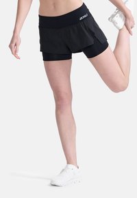 Čierne športové šortky s vrstveným dizajnom, s širokým elastickým pásom. Nosia sa s bielymi bežeckými topánkami, čo vytvára športový vzhľad.